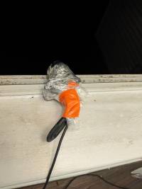 Picture of the webcam completely wrapped in plastic wrap secured by orange duct tape sitting on my window sill